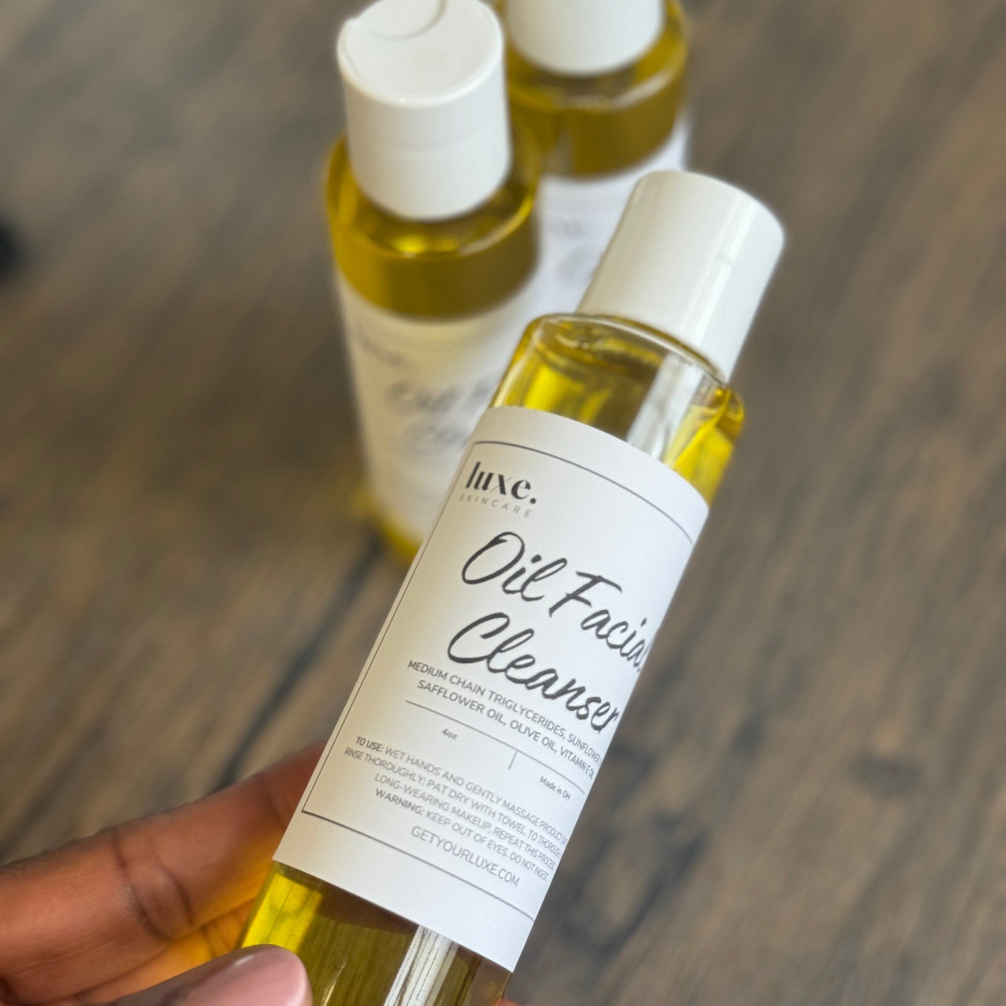 Oil facial cleanser bottles, clear glass with white label, Luxe brand visible, held in hand