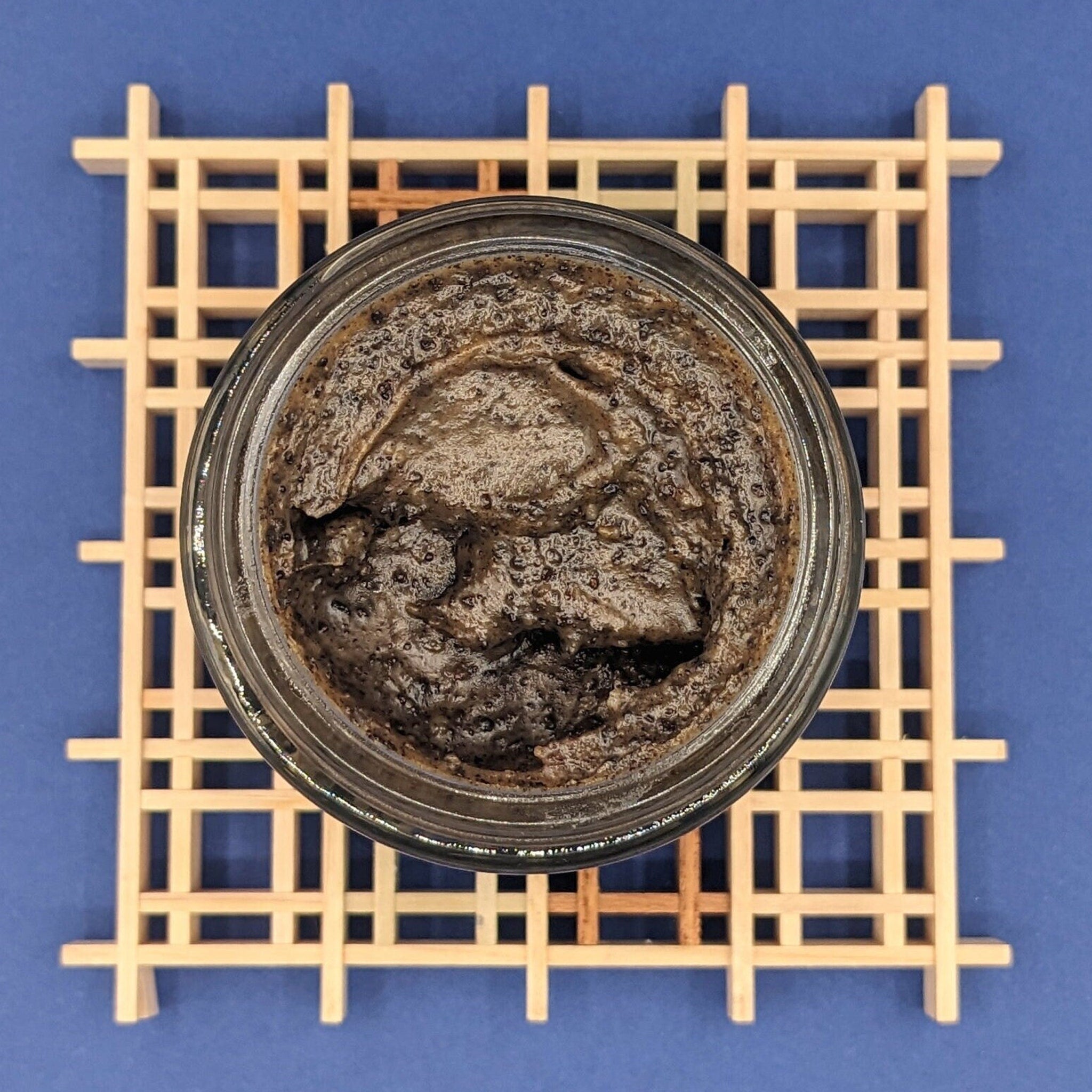 Coffee face scrub, dark brown emulsified texture in glass jar, on wooden grid