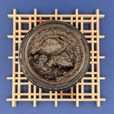 Coffee face scrub, dark brown emulsified texture in glass jar, on wooden grid