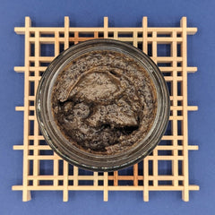 Coffee face scrub, dark brown emulsified texture in glass jar, on wooden grid