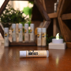 Lip balm tube with white, tan, and clear packaging, and Buffalo Bees logo on a wooden surface