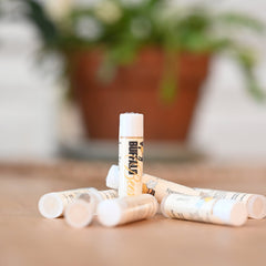 Lip balm tubes with white caps and Buffalo Bees branding, on a brown surface