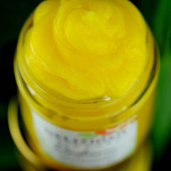 Yellow cream in glass jar, swirled texture, close-up view against green background