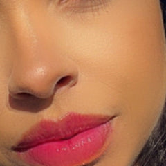 Lip gloss with pink color, glossy finish, and visible skin texture on face
