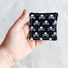 Square black fabric with white skull and crossbones pattern, held in hand