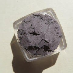 Powder eyeshadow in gray color with a cracked texture, inside a clear plastic container