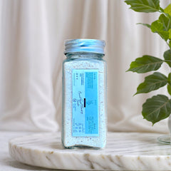 Facial Cleansing Powder in glass jar with blue label, on marble surface, with plant in background