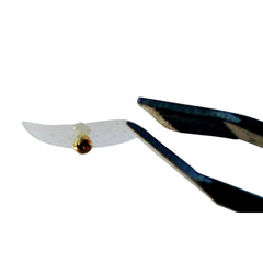 Tweezers holding a clear, perforated material with a gold bead, dark metal tool