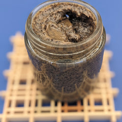Brown paste in a glass jar, textured surface, visible seeds, on a white structure with a blue background