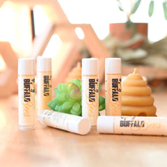 Lip balms, white tubes with Buffalo Bees branding, arranged on wood surface with succulent