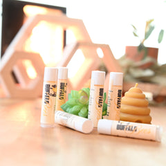 Lip balm tubes with white caps, beige tubes, and "Buffalo Bees" branding on a table