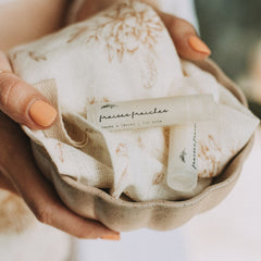 Lip balm tubes with "fraises fraiches" text, clear and white, on a floral patterned cloth in a ceramic bowl