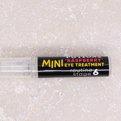 Eye treatment tube with black label, yellow text, and clear plastic applicator on stone surface