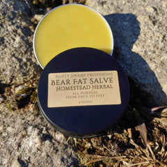 Bear fat salve with yellow balm, black lid, and Homestead Herbal label on rock surface