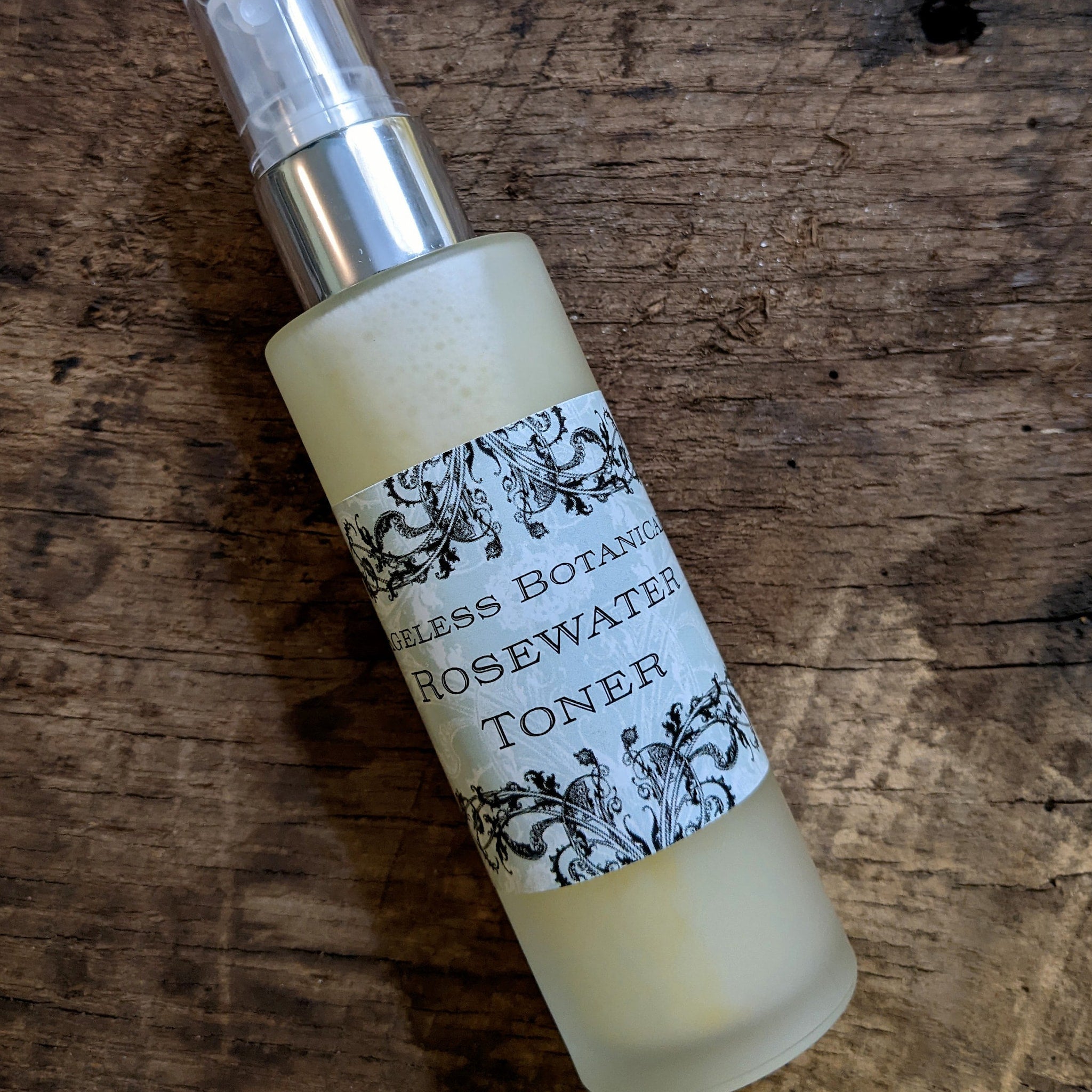 Rosewater toner bottle, frosted glass, silver pump, Ageless Botanicals label, on wood surface