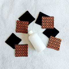 Makeup remover pads, black and orange fabric with geometric pattern, with white bottle on white towel