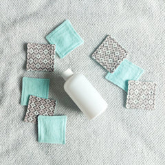 Makeup remover pads, fabric, square, patterned and teal, with bottle on towel
