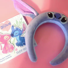 Stitch headband, blue plush with pink ears, and Disney Stitch eyeshadow palette on pink background