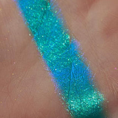 Eyeshadow swatch with teal shimmer, iridescent sheen, and textured surface on skin