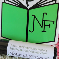 Natural Fiction lip balm with black tube and white label, green logo sticker in background