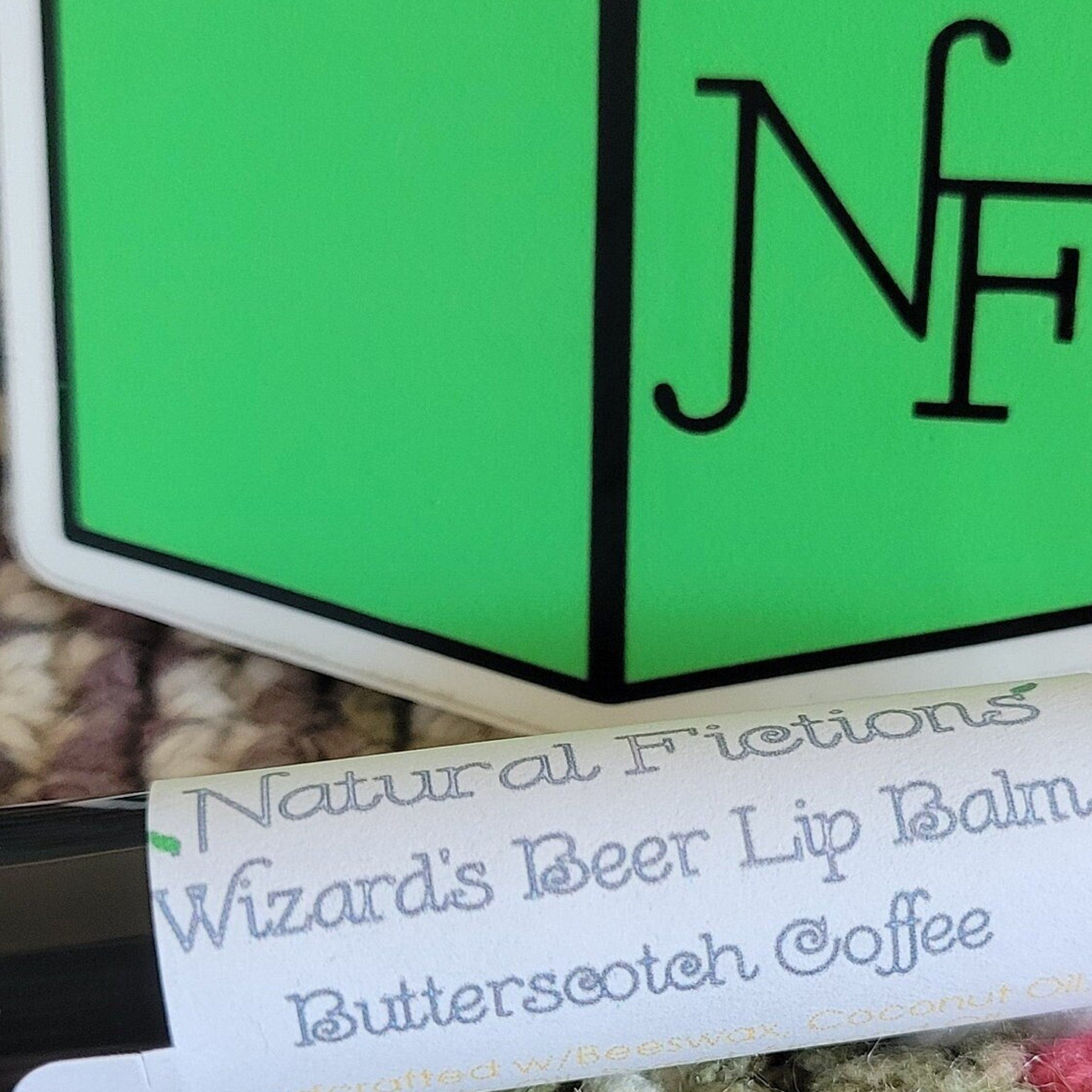 Lip balm with white label, green logo, and Natural Fictions text