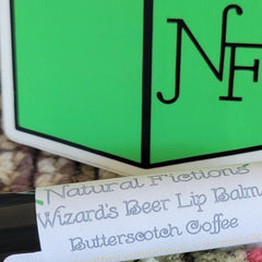Lip balm with white label, green logo, and Natural Fictions text