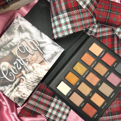 Eyeshadow palette with multiple colors in black case, plaid fabric and "Cozy Up" cover art