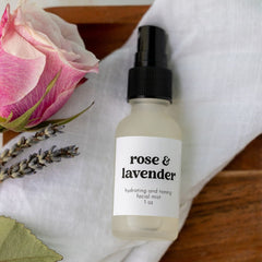 Facial mist bottle with white label, black cap, and "rose & lavender" text on white fabric