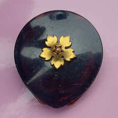 Round compact with dark tortoiseshell pattern, gold flower detail, and vintage style