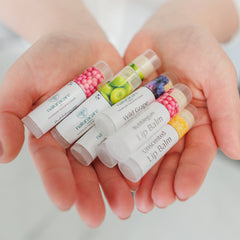 Natural lip balms in white tubes with fruit illustrations and Naturacare brand name, held in open hands