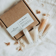 Lip balm set with clear tubes, brown box, and La Marcotterie branding on white fabric
