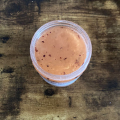 Orange-colored food with red flecks in clear plastic container on wood table