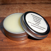 Lip balm in open silver tin with PrairieWoodSprite label, light yellow cream visible