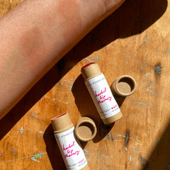 Lip balm tubes with red tint, brown paper, and text "PRIYA MEANS LOVE" on wooden surface