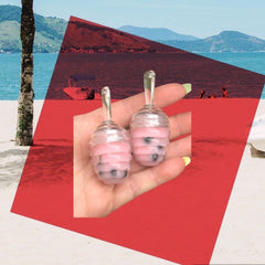 Lip gloss, pink and clear glass bottles, held in hand near beach scene