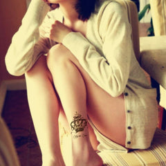 Tattoo design of a crown, black ink, on a leg, with text below it.