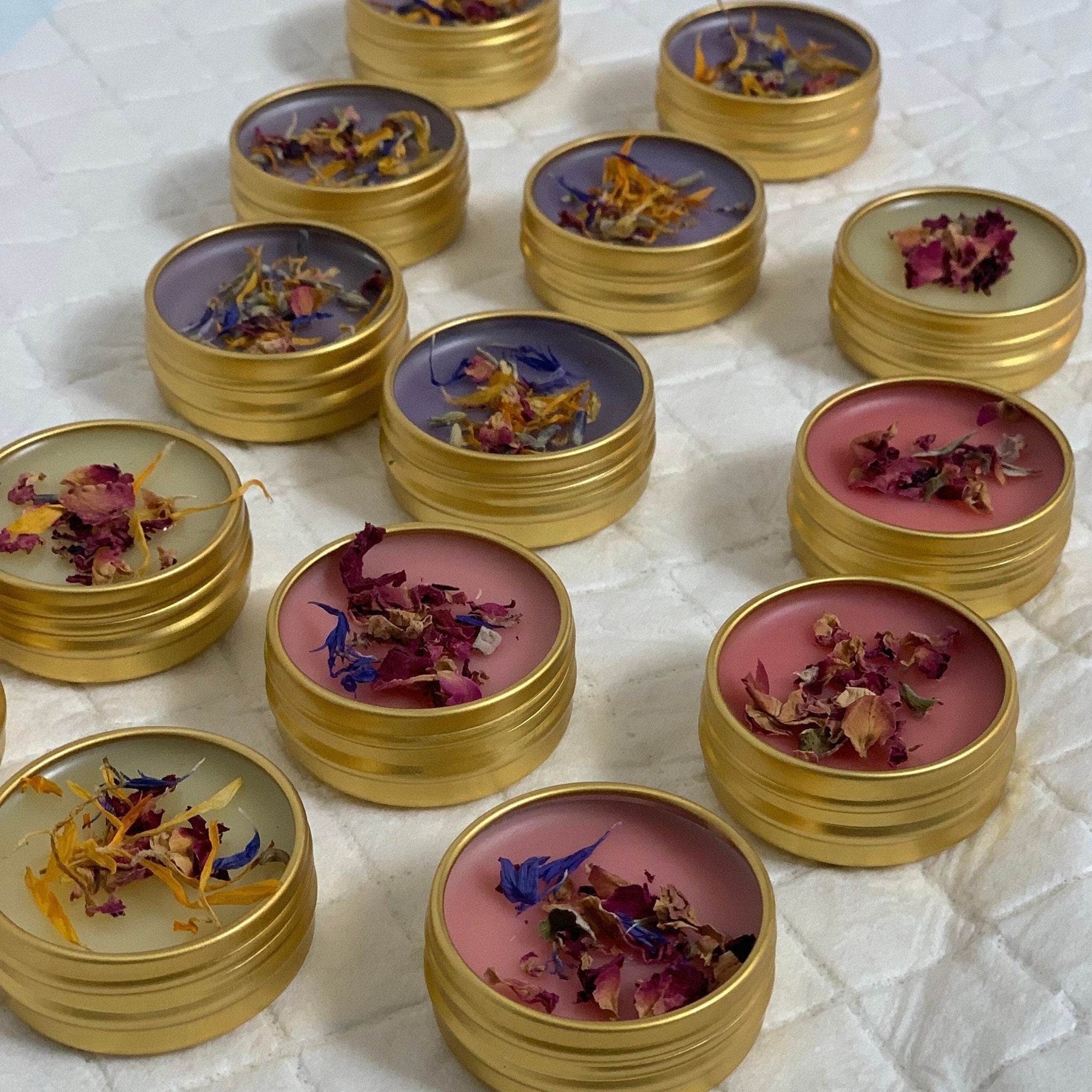 Lip balms in gold tins with various colors and dried flower toppings