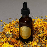 Calendula oil bottle brown glass with gold label, surrounded by yellow petals, Brilliant K Artisans