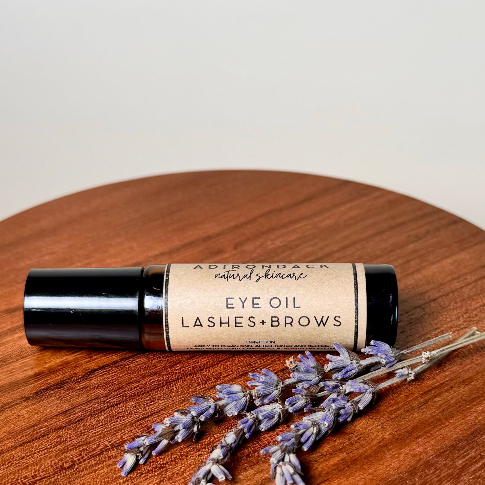Eyelashes and Eyebrows Serum Oil, black glass bottle with label, Adirondack Natural Skincare, lavender sprigs on wood