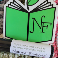 Lip balm with Natural Fictions label, black tube, white label, green book sticker, black text