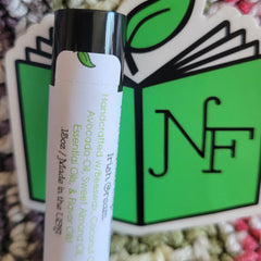 Lip balm tube with black cap and white label, green leaf logo, and "NF" on green background
