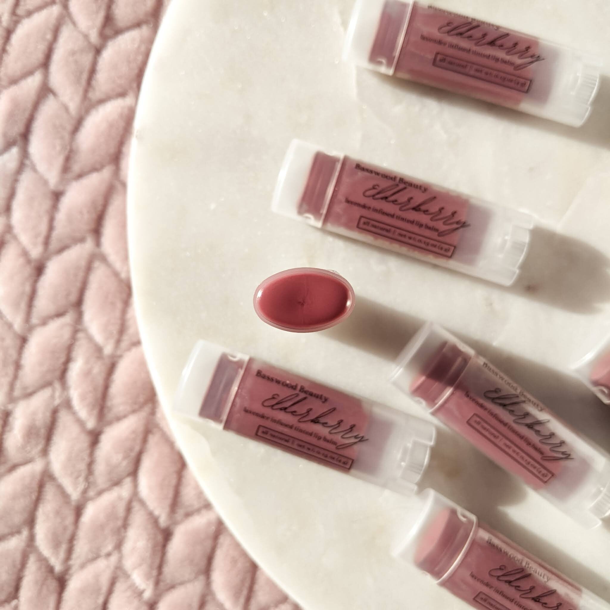 Lip balms, elderberry tinted, clear tubes, Basswood Beauty branding visible
