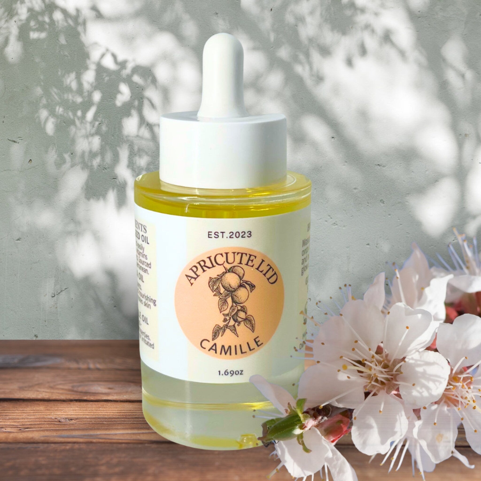 Skin care oil bottle, clear glass, white cap, Camille brand visible, flowers in foreground