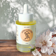 Skin care oil bottle, clear glass, white cap, Camille brand visible, flowers in foreground