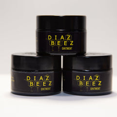 Ointment jars stacked, black containers with yellow "DIAZ BEEZ" logo and text, white background