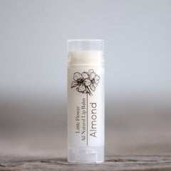 Lip balm tube with white label, black floral design, and "Almond" text.