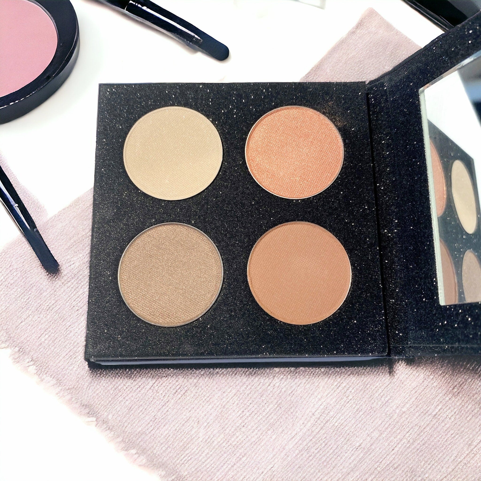 Eye shadow quad with four circular shades, black glitter palette, and mirror