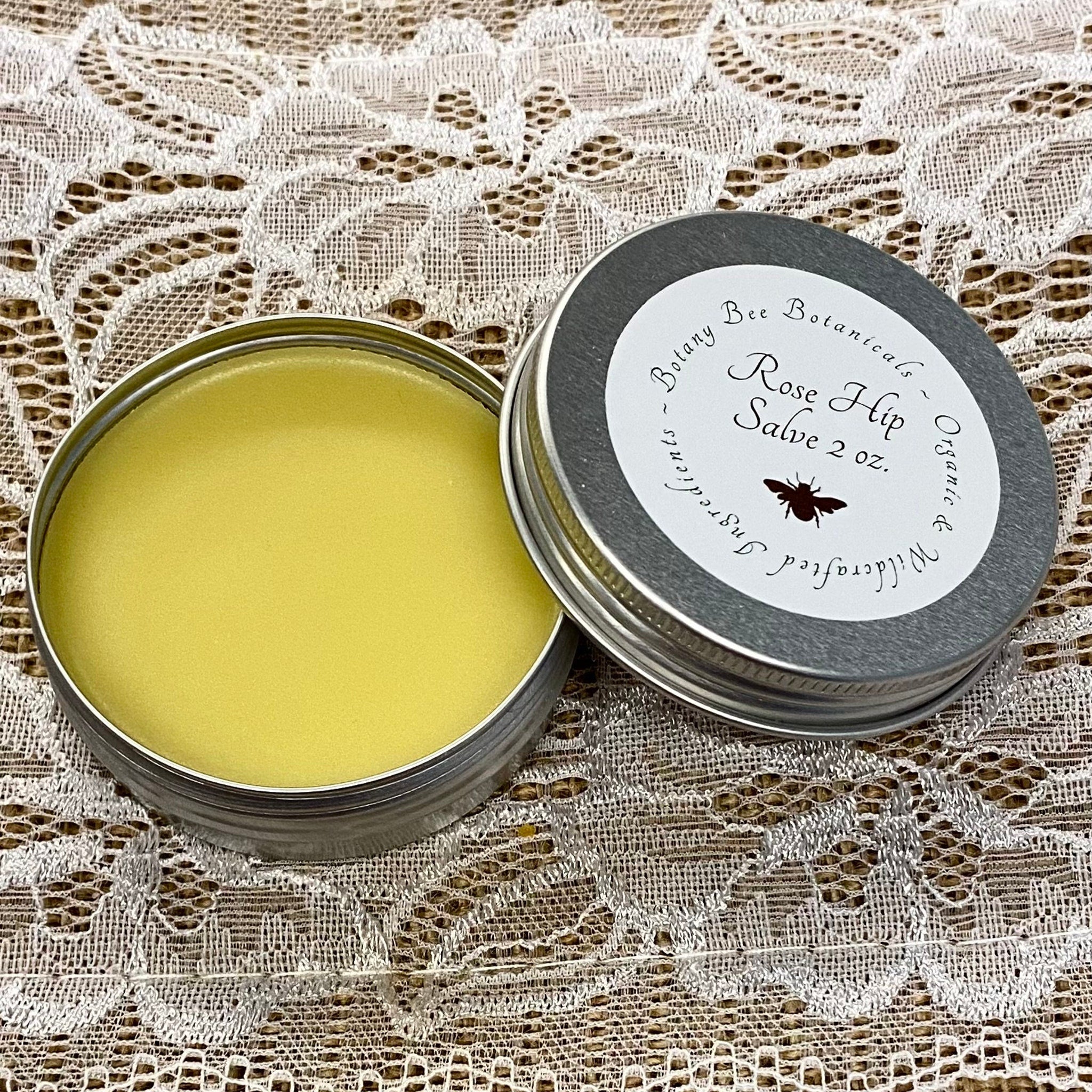 Rose Hip Salve in silver tin, yellow salve, Botany Bee Botanicals label on lid, lace background