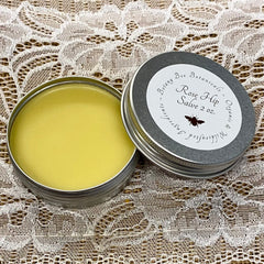 Rose Hip Salve in silver tin, yellow salve, Botany Bee Botanicals label on lid, lace background