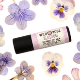 Lip balm tube with black base and floral label, surrounded by purple and white flowers